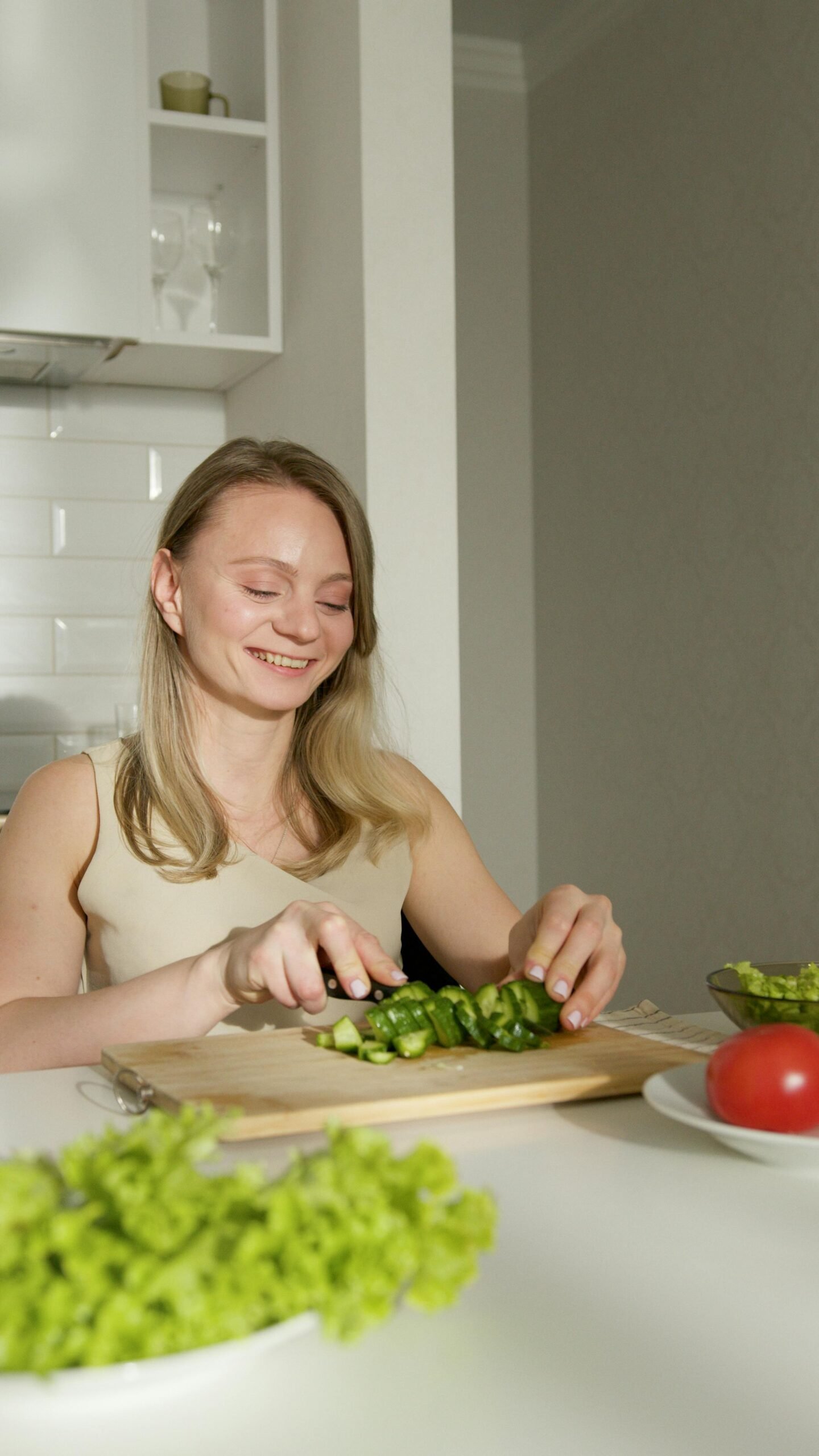 Young woman smiling while chopping vegetables indoors, focusing on healthy food preparation.